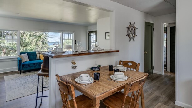 Un coin repas avec une table en bois dressée pour quatre personnes, un canapé bleu et une vue sur l’extérieur.