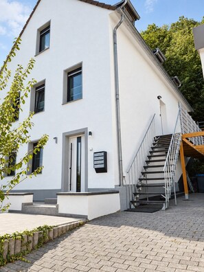 A white building with a staircase leading to a wooden deck. - JUPAS° Studio21 – Terrace with Hanging Nest (Trier)