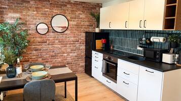 Cocina moderna con armarios blancos, pared de ladrillo, mesa de comedor con sillas y una planta pequeña.