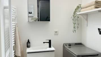 Un baño moderno con tocador blanco, espejo, perchero, lavamanos, inodoro y un pequeño cubo de basura.
