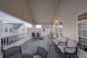 A covered outdoor patio with lounge chairs and a table, overlooking a residential area. - The Loft! The space with a large pool, game room, relaxing space upstairs. (Hurricane)
