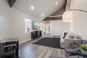 A spacious living room with a grey sofa, a gaming console, and a TV. - The Loft! The space with a large pool, game room, relaxing space upstairs. (Hurricane)