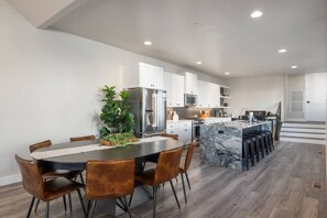 A modern kitchen with white cabinets, a marble island, and a dining area with a round table and chairs.