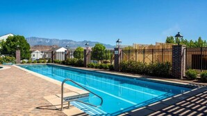 Una piscina con vistas despejadas a montañas al fondo, rodeada por un patio de ladrillo y una valla de madera.