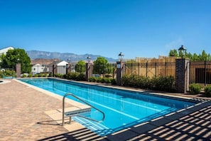 A swimming pool with a clear view of mountains in the background, surrounded by a brick patio and a wooden fence. - The Loft! The space with a large pool, game room, relaxing space upstairs. (Hurricane)