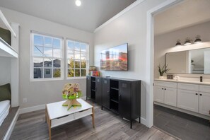A modern kitchen with white cabinets, a large window, and a flat-screen TV mounted above the counter. - The Loft! The space with a large pool, game room, relaxing space upstairs. (Hurricane)