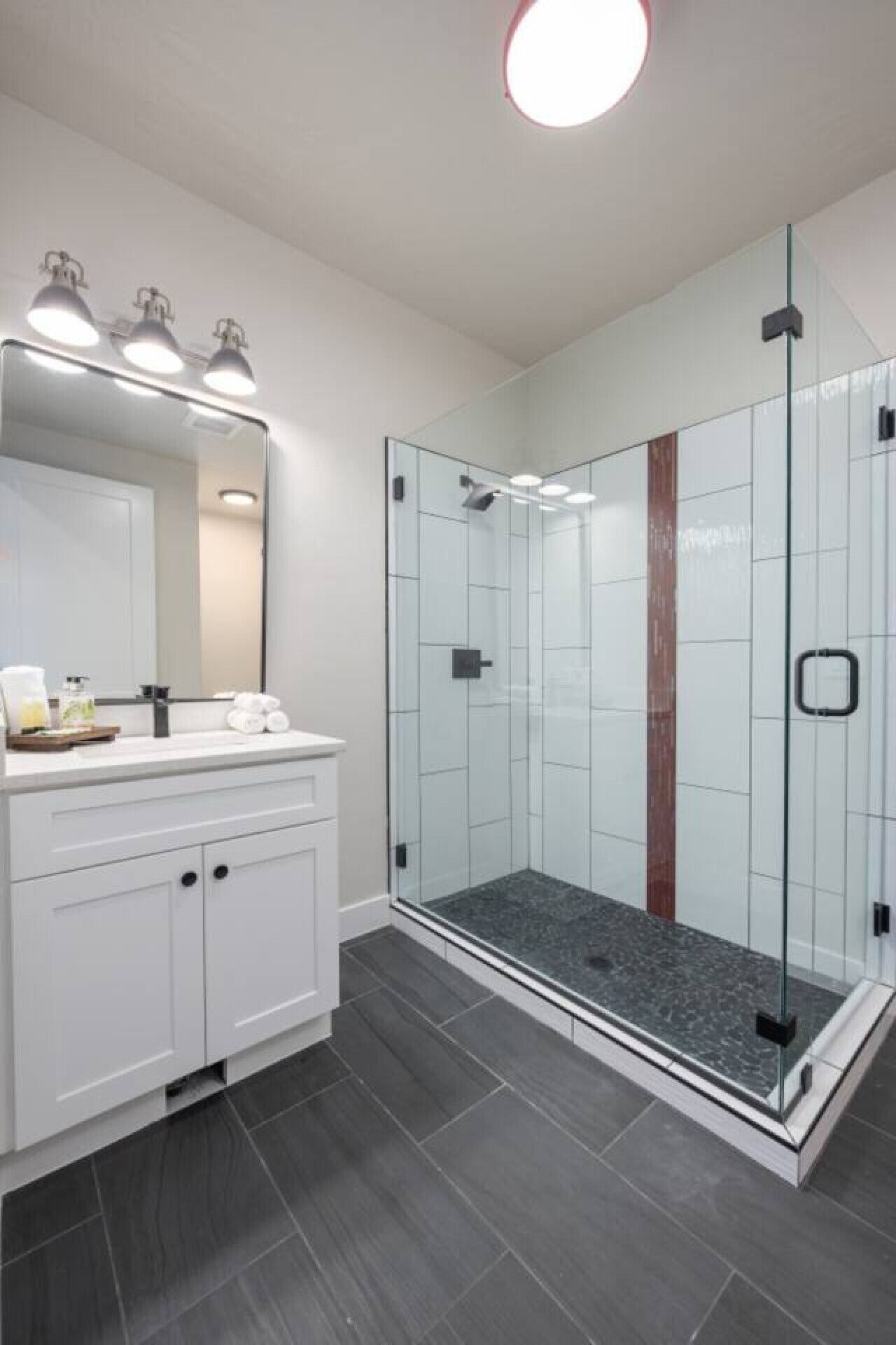 A modern bathroom with a glass-enclosed shower, white cabinetry, and a large mirror with overhead lighting.