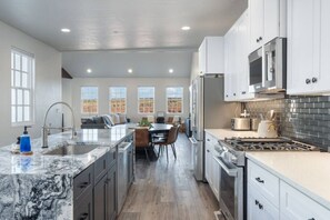 A spacious kitchen with a central island, white cabinetry, stainless steel appliances, and a view through large windows.