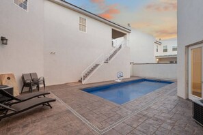 A swimming pool with a white wall and a staircase leading to a balcony.