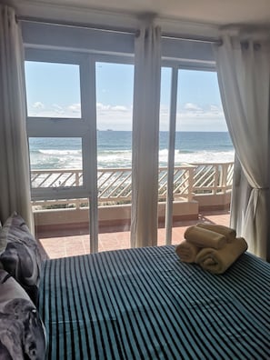 Quarto com cama, vista para o oceano e varanda com grades.