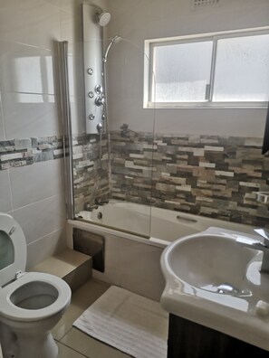 A bathroom with a glass-enclosed shower, a bathtub, a toilet, and a sink. - 15 Isikhulu (eMdloti)