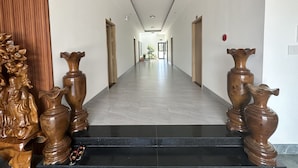 Un long couloir étroit, doté d’un sol noir poli et de murs blancs. De part et d’autre de l’entrée, on peut admirer des sculptures en bois.