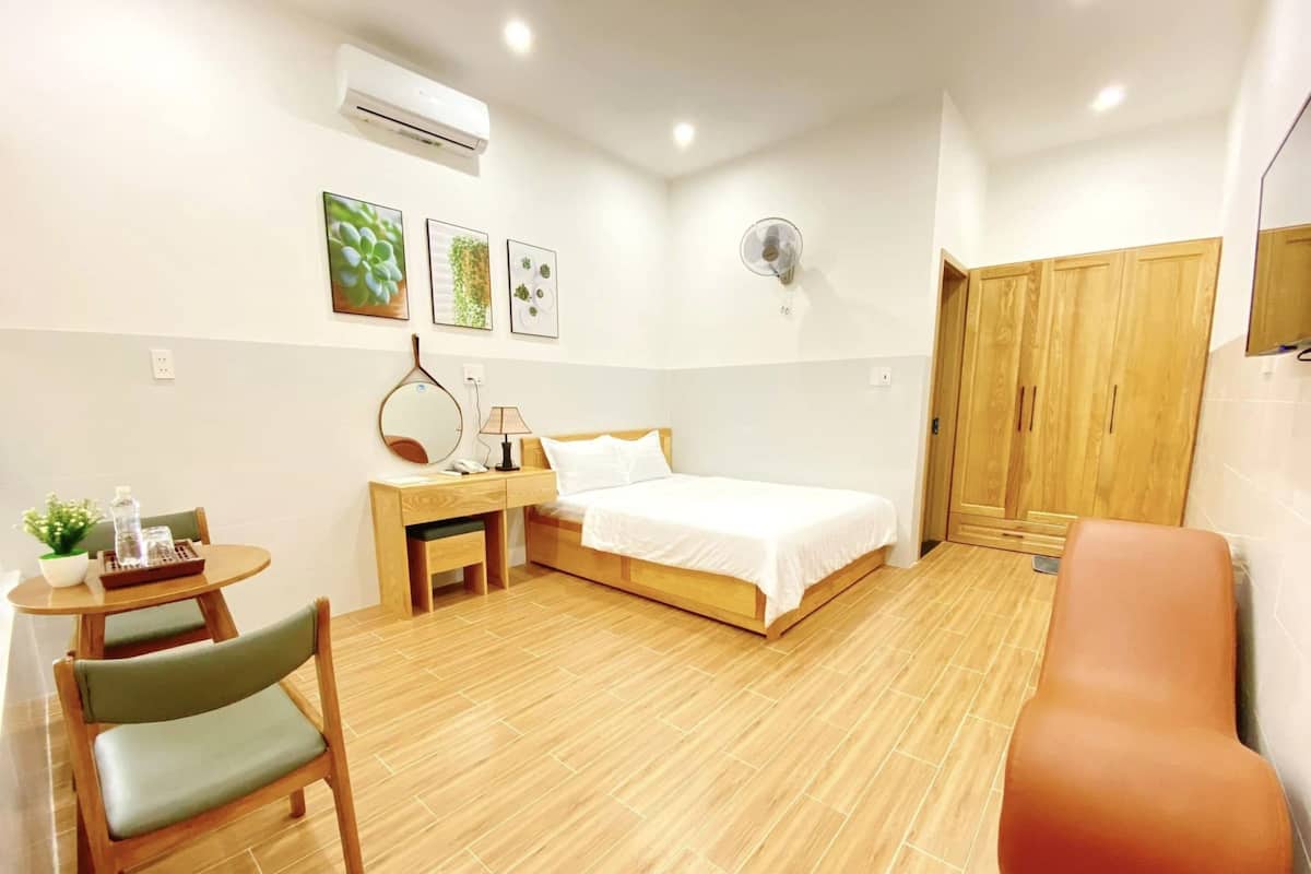 Ein Hotelzimmer mit einem Bett, einem Schreibtisch mit Stuhl, einem kleinen Tisch mit Pflanze und einem Kleiderschrank.