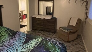 Quarto com cama, penteoudeiro, cadeira e espelho.