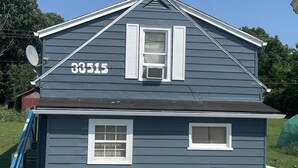 Uma casa de dois andares com fachada azul escura, detalhes brancos e o número '33515' na frente.
