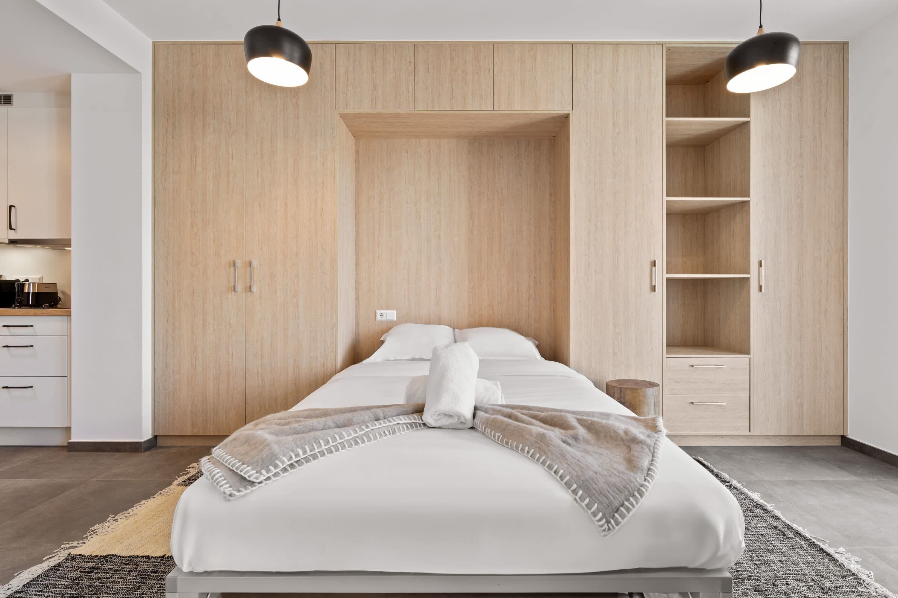 Une chambre moderne avec un lit, une armoire en bois et des lampes suspendues.