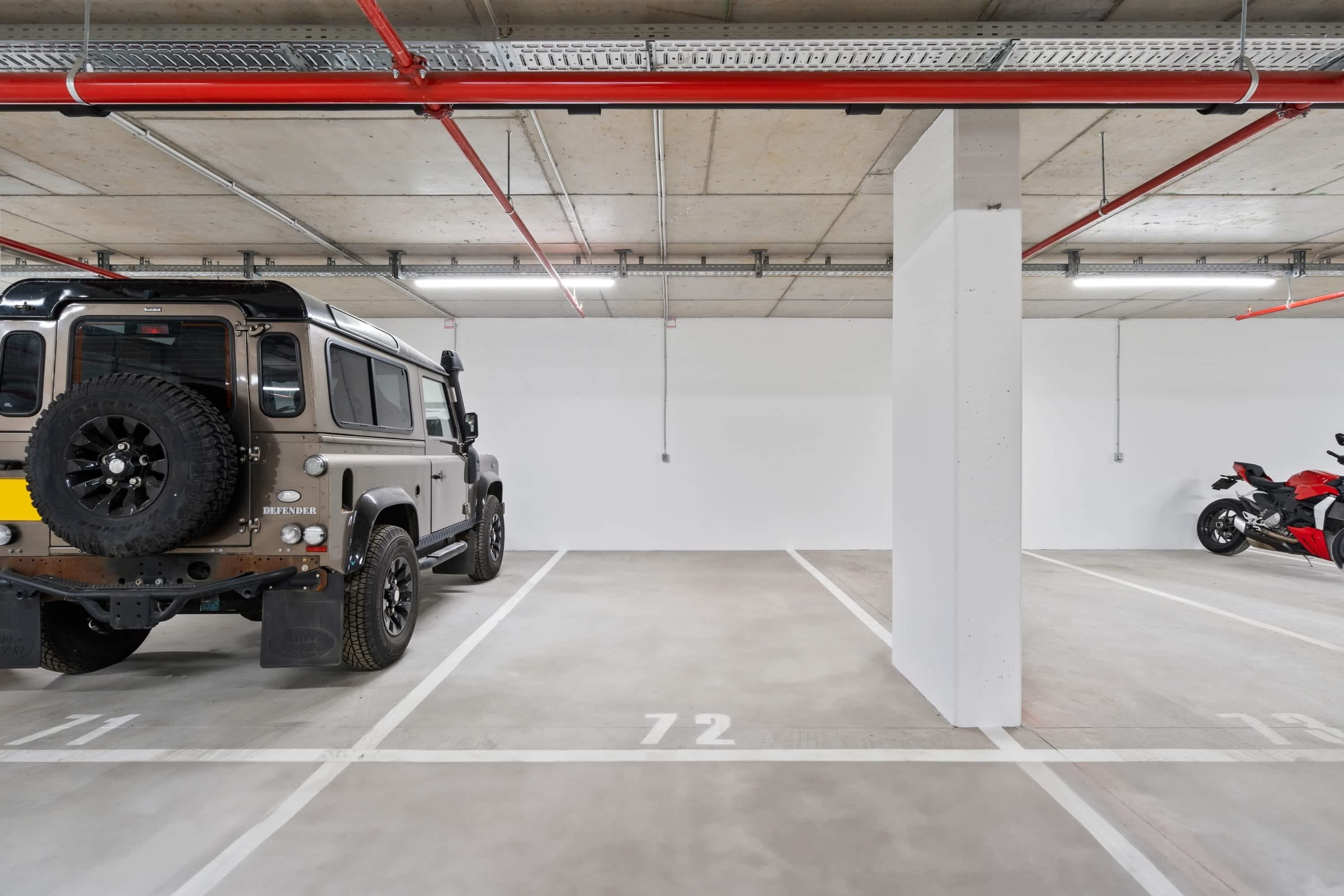 Un parking où sont garés un Jeep Defender et une moto rouge.