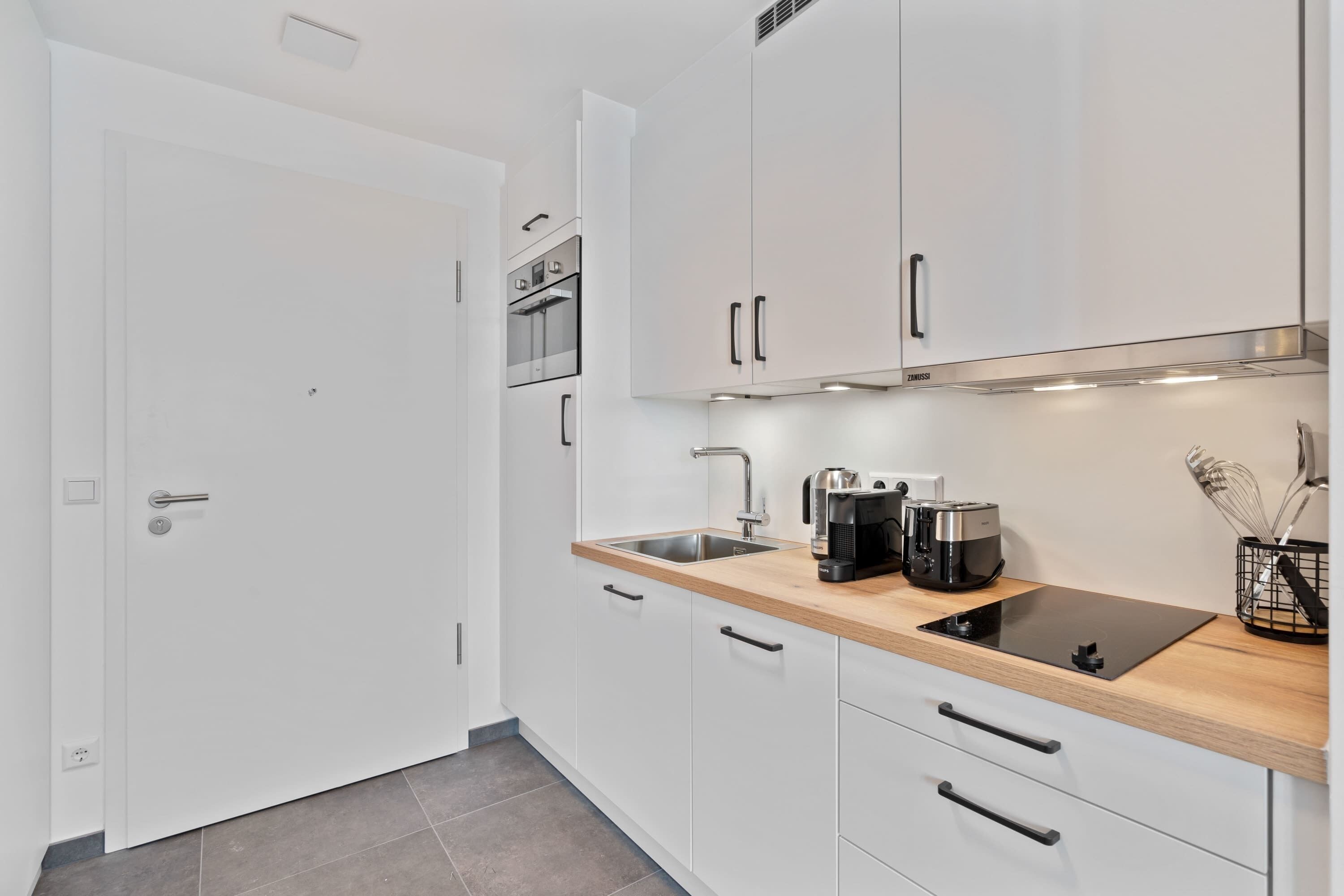 A modern kitchen with white cabinets, a stainless steel sink, and a wooden countertop.