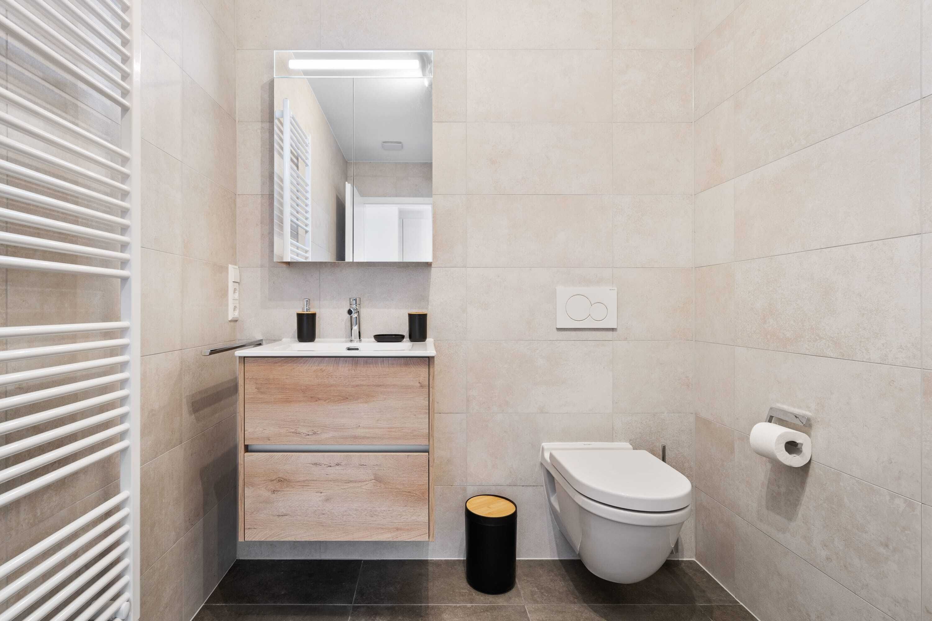 A modern bathroom with a white toilet, a sink with a mirror above it, and a black trash bin.