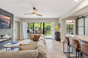 A modern living room with a fireplace, a sofa, a dining area with bar stools, and a large sliding glass door leading to an outdoor patio. - Lake Life Location with Serenity (Osage Beach)
