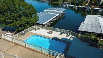 A swimming pool with a deck, surrounded by a wooden fence, and docked boats in a calm lake.