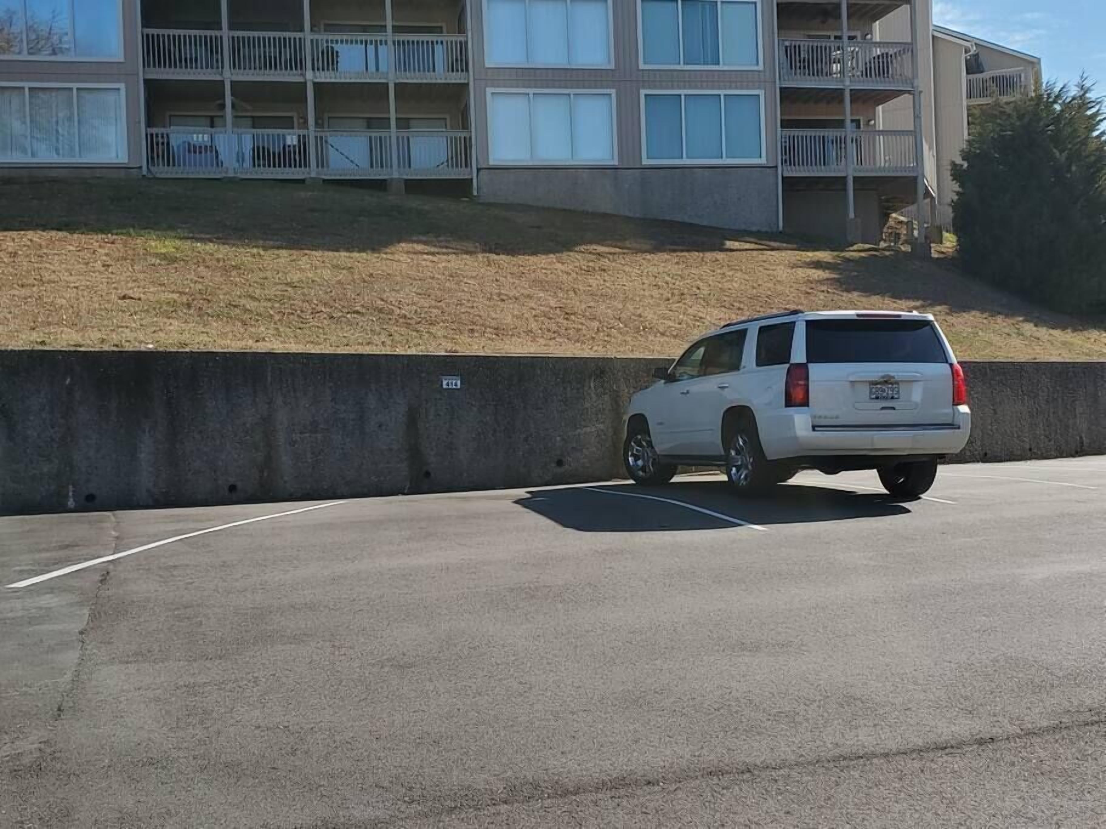 A white SUV parked in a parking lot with a concrete wall and a building in the background.