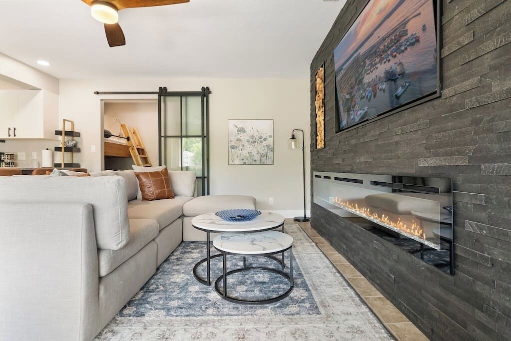 A modern living room with a fireplace, a sofa, two round tables, and a large painting on the wall.