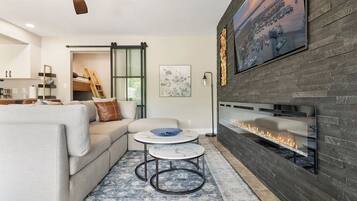 A modern living room with a fireplace, a sofa, two round tables, and a large painting on the wall.