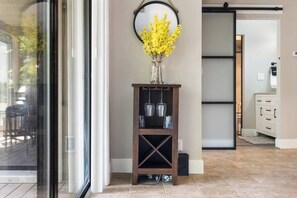 Une pièce avec une porte vitrée, une console en bois sur laquelle est posé un vase rempli de fleurs jaunes, et un miroir accroché au mur.