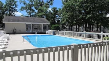 Une piscine avec une terrasse en bois, un espace salon couvert et une zone délimitée par une clôture.