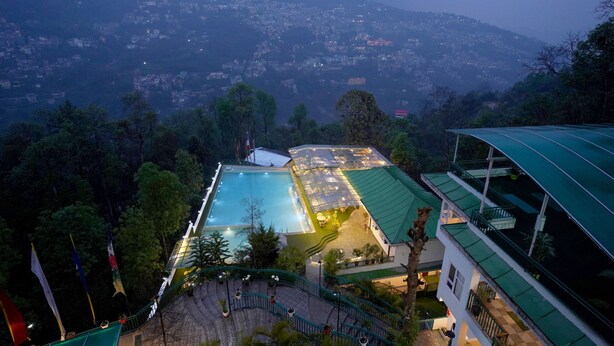 Un hotel con piscina, rodeado de exuberante vegetación y vistas a un paisaje montañoso.