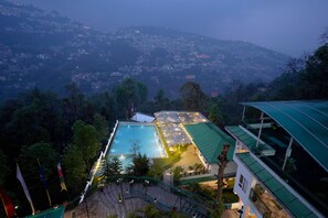 A hotel with a swimming pool, surrounded by lush greenery and a view of a mountainous landscape. - Treenz Hotels (Gangtok)