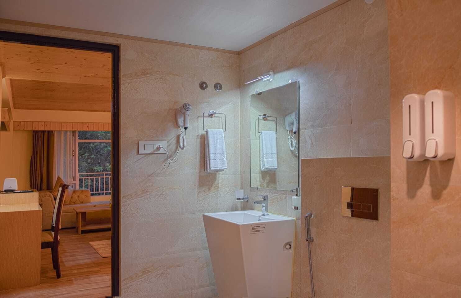 A modern bathroom with a large mirror, a sink, and a shower. There is a wooden door leading to a balcony with a sofa and a table.