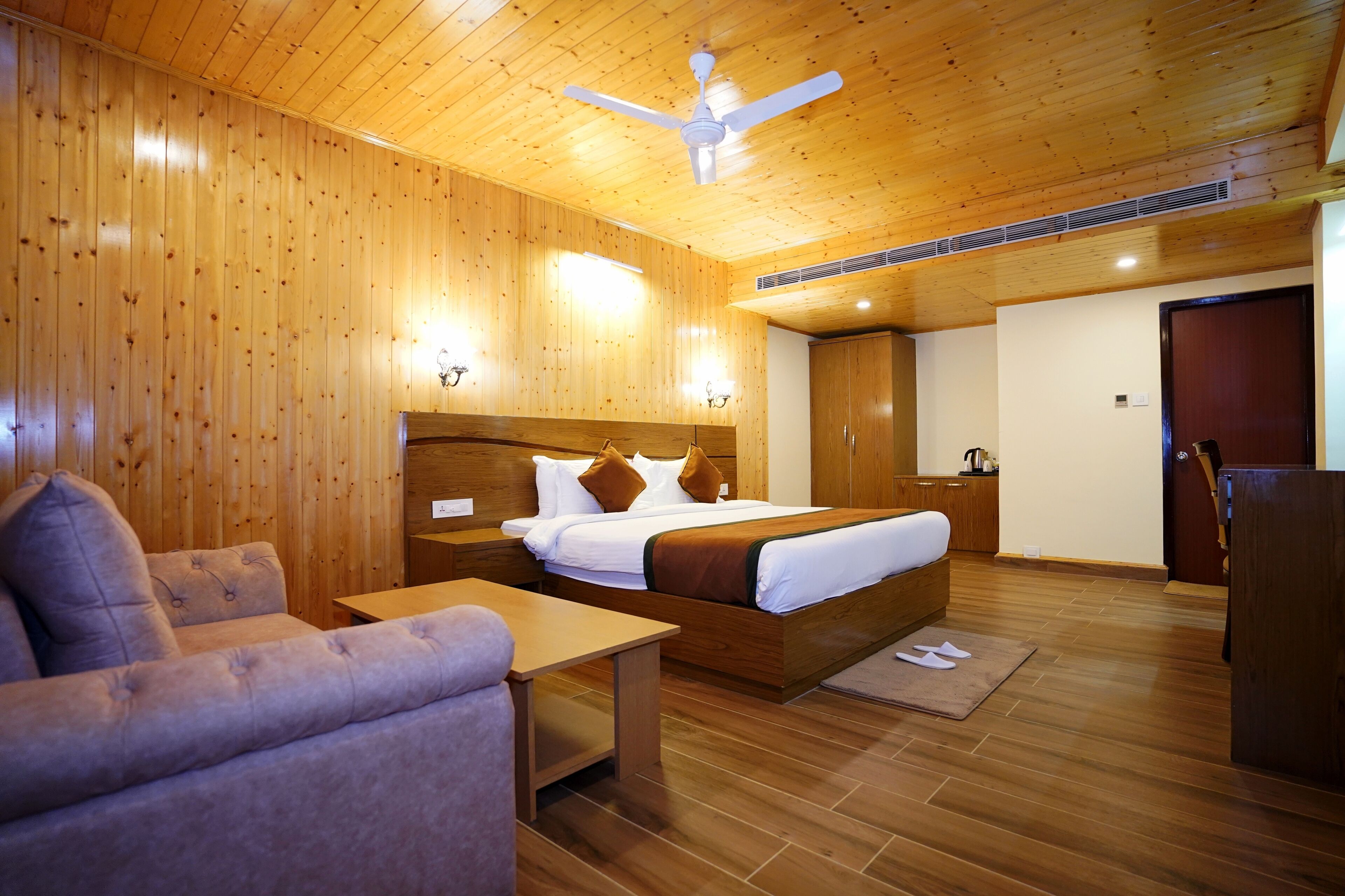 A wooden-paneled room with a bed, a sofa, a table, and a ceiling fan.