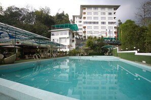 Una piscina con fondo de cristal, rodeada de sillas de descanso y una zona cubierta con techo verde.