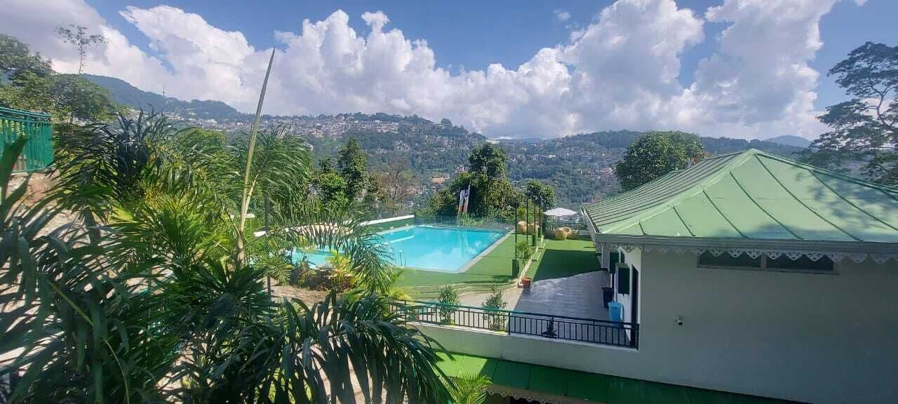 Une piscine offrant une vue sur un paysage montagneux, entourée de verdure et bordée d’un bâtiment doté d’un toit végétalisé.