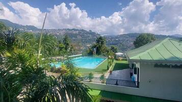 Une piscine offrant une vue sur un paysage montagneux, entourée de verdure et bordée d’un bâtiment doté d’un toit végétalisé.