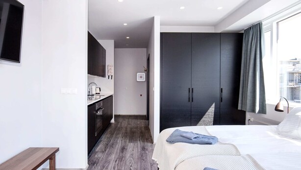 A modern hotel room with a bed, a desk, a kitchenette, and a large wardrobe. - Svala Downtown Studio Twin beds (Reykjavík)
