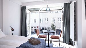 A modern hotel room with a large bed, a round table with two chairs, a view of the city through large windows, and a skylight. - Svala Downtown Studio Queen bed (Reykjavík)