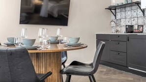 Un espace repas moderne avec une table ronde en bois, des chaises noires et un téléviseur fixé au mur.
