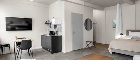 Una habitación de hotel moderna con cama, escritorio con silla, kitchenette pequeña y televisor montado en la pared.