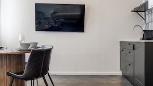 A modern kitchen with a flat-screen TV mounted on the wall, a dining table with chairs, and a built-in sink.
