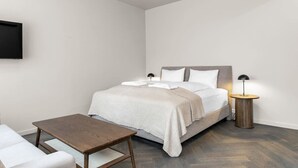 A modern bedroom with a bed, bedside tables, a small table, and a TV mounted on the wall.