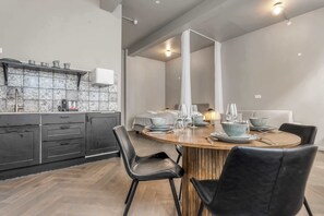 A modern kitchen with dark cabinets, a marble backsplash, and a dining area with a wooden table and black chairs.