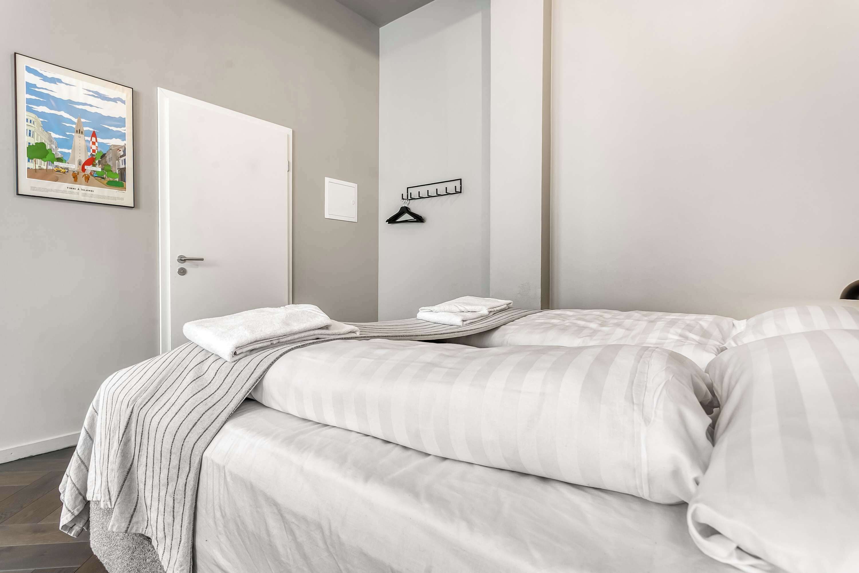 Ein Hotelzimmer mit einem Bett, einer Tür, einem Kleiderhaken und einem gerahmten Bild an der Wand.