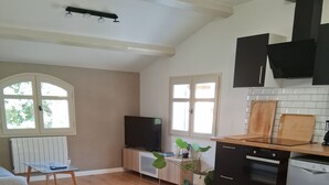 A modern kitchen with a dining area, wooden flooring, and a TV on a cabinet. - Appartement T2 Dans Villa à la Campagne (Solliès-Toucas)