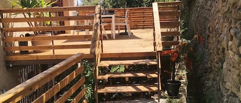A wooden deck with a table and chairs, surrounded by a stone wall and greenery.