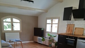 A modern kitchen with wooden flooring, a dining table with chairs, a TV, and a window with blinds. - Appartement T2 Dans Villa à la Campagne (Solliès-Toucas)