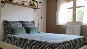 A bedroom with a bed, pillows, a hanging light fixture, a window with curtains, and a radiator. - Appartement T2 Dans Villa à la Campagne (Solliès-Toucas)