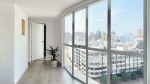 Ein geräumiges Zimmer mit großen, vom Boden bis zur Decke reichenden Fenstern, Holzboden und einer Topfpflanze.